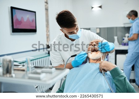 Male dentist using dental drill while working on mature patient's teeth.  Royalty-Free Stock Photo #2265430571