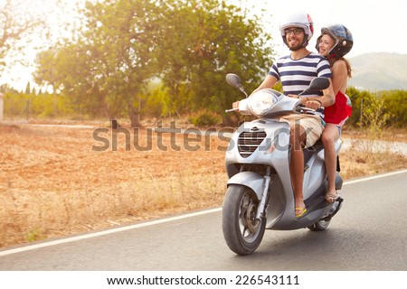 Young Couple Riding Motor Scooter Along Country Road Royalty-Free Stock Photo #226543111