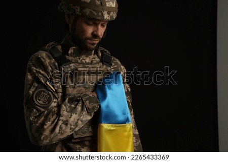 Soldier in military uniform with Ukrainian flag on black background