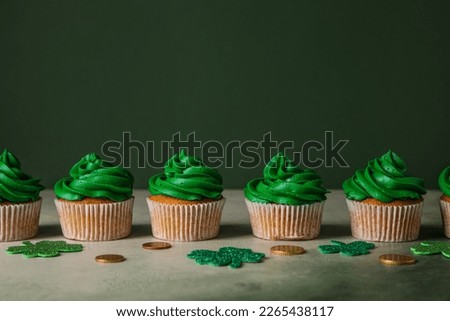 Tasty cupcakes for St. Patrick's Day, clovers and coins on grunge table against green background