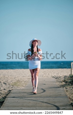 Woman with vitiligo smiling while using mobile phone walking on walkway at the beach.