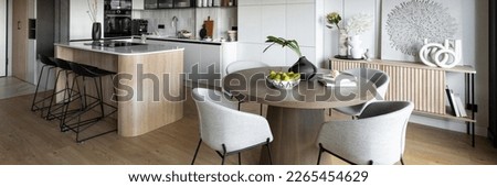 Contemporary design of dining room interior with round table, gray chairs, wooden floor, decorations, flowers in vase, paintings and elegant personal accessories. Stylish home decor. Template.
