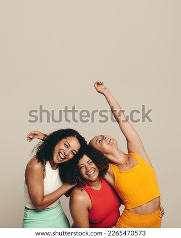Three young women laughing happily as they stand together in a studio wearing sports clothing. Group of female friends celebrating their fit, healthy and sporty lifestyle. Royalty-Free Stock Photo #2265470573