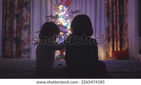 Little kids silhouettes in front of Christmas tree at home enjoying Silent Night