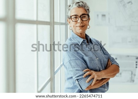 Empowered female designer standing in her office and looking at the camera. She is a mature and confident business woman with experience and expertise in her work as a design architect. Royalty-Free Stock Photo #2265474711
