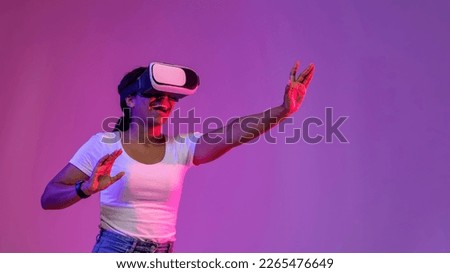 Cheerful Black Female Experiencing Virtual Reality In Vr Glasses While Standing Under Neon Lighting Over Purple Studio Background, Excited African American Woman Enjoying Modern Technologies