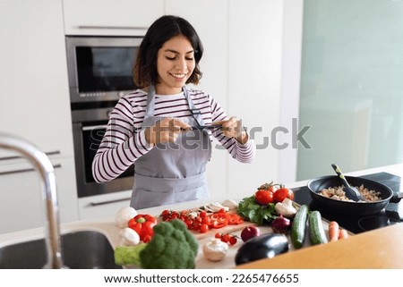 Food blogging concept. Positive pretty young arab woman taking photo of healthy vegetables on cellphone, cooking fresh salad while standing in kitchen. Nutrition and weight loss blog concept