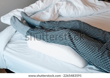 a man in bed leans his legs on a leg elevation pillow made of memory foam Royalty-Free Stock Photo #2265483591