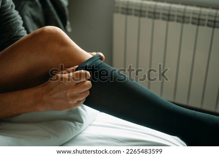 closeup of a man putting on a compression sock sitting on the bed at home