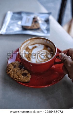 hand holding a red cup filled with coffee latte, and a cookie. isolated