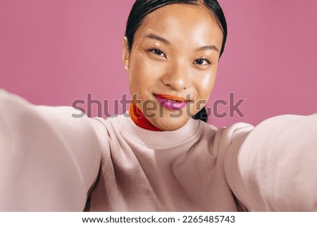 Female looking at the camera while taking a selfie in a studio, she is wearing a bold two tone lipstick. Woman in her 20’s enjoying her new makeup look in a studio. Royalty-Free Stock Photo #2265485743