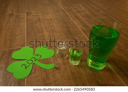 shot and pint glasses on wooden bar background filled with green spirit beer and shamrock, drunk at celebration for St Patrick's day 2023. Irish holiday popular drinking event when people party