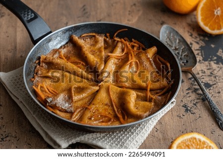 Traditional French Crêpes suzette pancakes with orange sauce in a pan on a wooden background. Selective focus Royalty-Free Stock Photo #2265494091