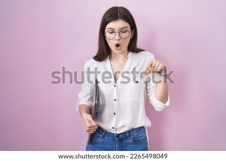 Young caucasian woman holding laptop pointing down with fingers showing advertisement, surprised face and open mouth 