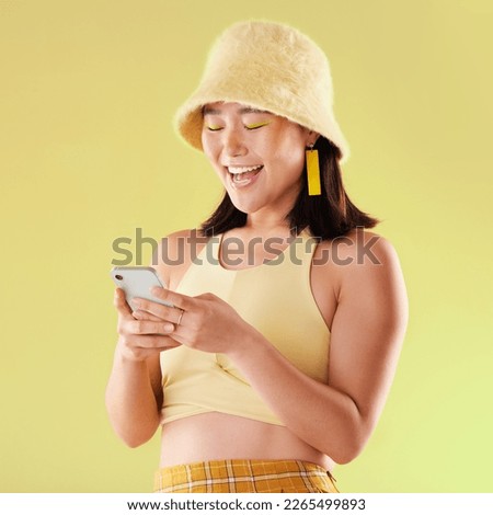 Phone, laughing and Asian woman typing in studio isolated on a yellow background. Comic emoji, technology and happy female model laugh at funny meme with mobile smartphone for social media or texting
