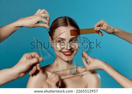 Young happy beautiful woman, female patient with human hands holding ruler isolated on blue studio background. Lifting concept. Correction of asymmetry. Royalty-Free Stock Photo #2265512957