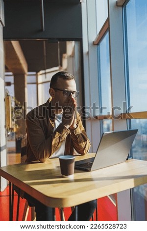 A balanced man in glasses and casual clothes works on a laptop from a cozy workspace. A successful freelancer works remotely. Royalty-Free Stock Photo #2265528723