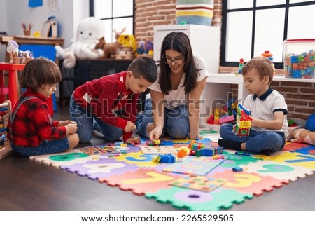 Teacher with group of boys playing with maths puzzle game sitting on floor at kindergarten Royalty-Free Stock Photo #2265529505