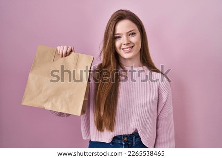 Young caucasian woman holding shopping bag and credit card looking positive and happy standing and smiling with a confident smile showing teeth 