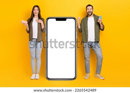 Full body photo of excited crazy people raise fists in triumph stand near huge phone display isolated on yellow color background