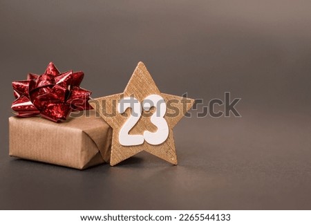 Greeting card for the Defender of the Fatherland Day. White, gold, red stars, a gift box and the number 23 on a brown background. The holiday is February 23.