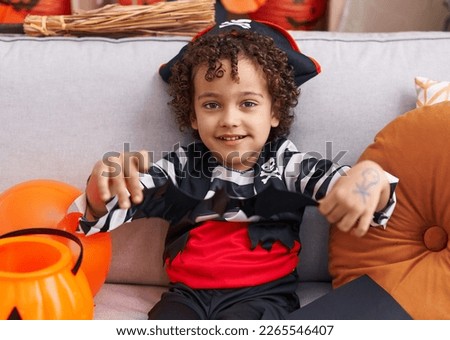Adorable hispanic boy having halloween party holding bat paper at home