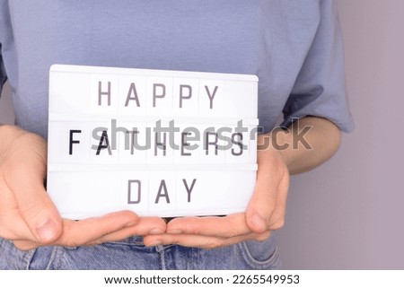 Happy Fathers Day. Female hands hold lightbox with letters in front of blue background. Festive concept.
