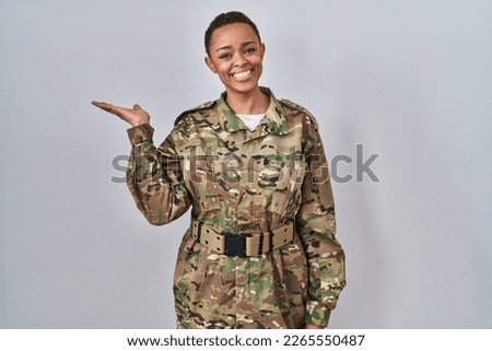 Beautiful african american woman wearing camouflage army uniform smiling cheerful presenting and pointing with palm of hand looking at the camera. 