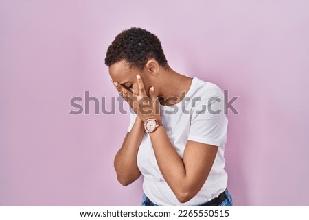 Beautiful african american woman standing over pink background with sad expression covering face with hands while crying. depression concept. 