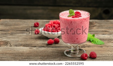 Yogurt smoothie with raspberries in glass on wooden table
