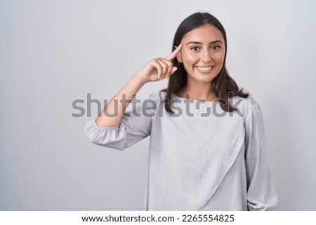 Young hispanic woman standing over white background smiling pointing to head with one finger, great idea or thought, good memory 