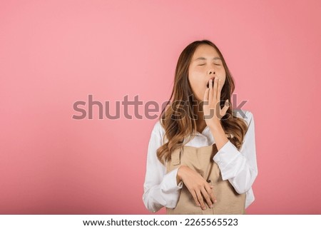 Portrait Asian beautiful young woman wearing overalls emotions tired and sleepy her yawning covering mouth open by hand, studio shot isolated on pink background, Female attractive insomnia boring Royalty-Free Stock Photo #2265565523