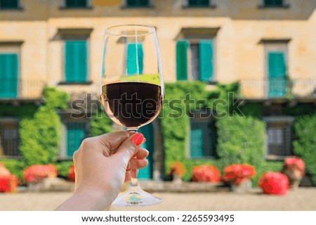 Woman s hand holding a glass of red Chianti wine at a vineyard with an ivy covered stone house at a vineyard in the famous Tuscany region, Italy Royalty-Free Stock Photo #2265593495