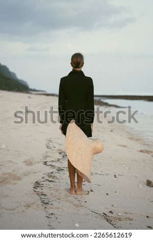 Young woman in a big straw hat on the ocean at sunset.