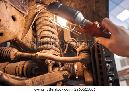 A car mechanic inspects springs, shock absorbers and suspension with a flashlight. Car on a repair stand. Technical service station for car.