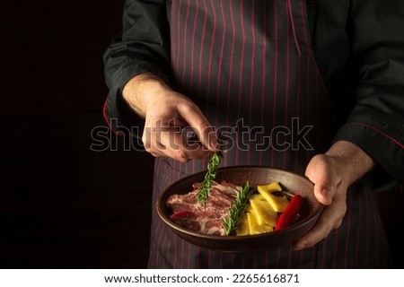 The cook puts rosemary on a plate with sliced steak and cheese. The concept of serving dishes to order by a waiter with a place for advertising on a black background.