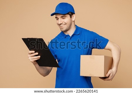 Delivery guy employee man wearing blue cap t-shirt uniform workwear work as dealer courier hold clipboard with papers document cardboard box isolated on plain light beige background. Service concept Royalty-Free Stock Photo #2265620141