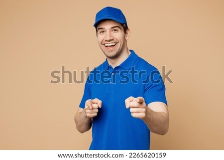 Delivery guy employee man wear blue cap t-shirt uniform workwear work as dealer courier point index finger camera on you motivating encourage isolated on plain light beige background. Service concept Royalty-Free Stock Photo #2265620159