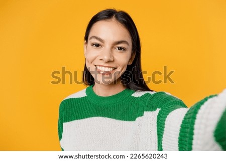 Close up young fun brunette latin woman wear casual cozy green knitted sweater doing selfie shot pov on mobile cell phone isolated on plain yellow background studio portrait People lifestyle concept