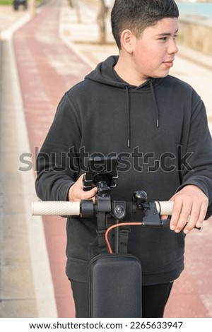 young teenager with a sideways glance riding an electric skateboard and using a smartphone application