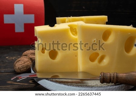 Block of Swiss medium-hard yellow cheese emmental or emmentaler with round holes and cheese knife and flag of Switzerland close up Royalty-Free Stock Photo #2265637445