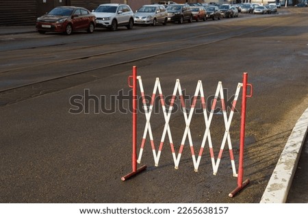 Restrictive temporary fence of red and white color in a parking area on a city street.