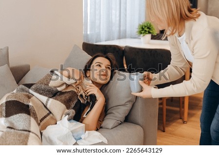 A mother takes care of her sick daughter, brings her warm tea to bed, and strokes her head. Royalty-Free Stock Photo #2265643129