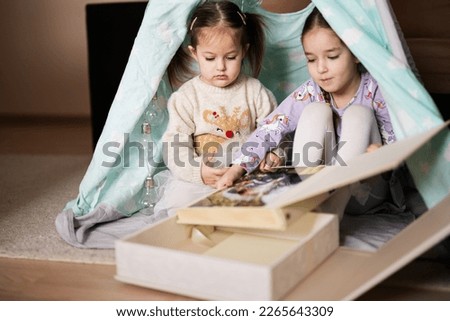 Two girls sisters at wigwam tent looking at parents wedding album.