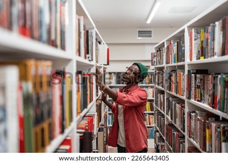 Thoughtful Black student guy searching materials for educational research in college library. Young African man choosing book for reading in bookstore, selective focus. Literature and education Royalty-Free Stock Photo #2265643405