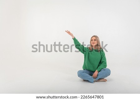 portrait of a young emotional girl flirtatiously stretching her arms to the side, gesturing with her hands, empty space, wearing jeans and a green sweater on an isolated white background