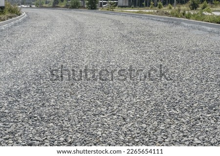 laying a new road, filled with gravel and crushed stone. macadam during road construction. Granite gravel of macadam, rock gray crushed for construction on the ground. background. Gravel fragments. Royalty-Free Stock Photo #2265654111