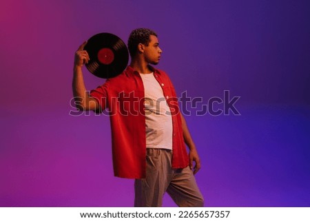 Young african guy posing with vinyl record isolated over purple neon studio background