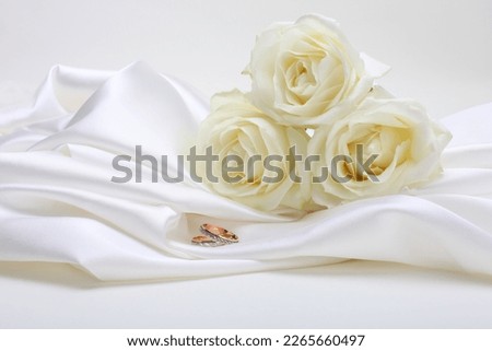 Nacre wave fabric silk with white rose flower bouquet and wedding ring. Abstract texture horizontal copy space background.