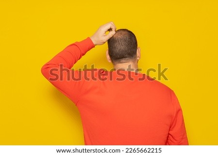 Back view of thoughtful man scratching his head over yellow background. He is doubting his existence, he does not understand the reason for life and what meaning it has. Royalty-Free Stock Photo #2265662215